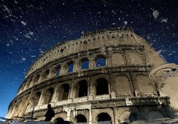 The coliseum is reflected in a puddle after the rain