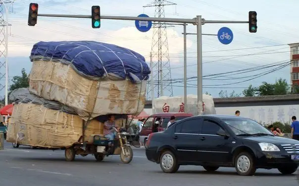 A man drives an overloaded three-wheeled motorcycle on a busy street in Beijing